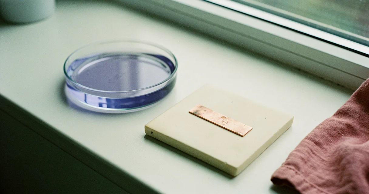 A shallow dish of blue-violet liquid and a copper strip on a cream laboratory bench in daylight